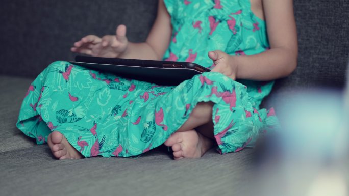 小女孩在家里客厅的沙发上使用平板电脑