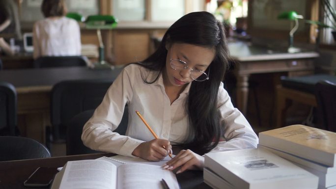 女学生穿着白衬衫在图书馆学习，做笔记