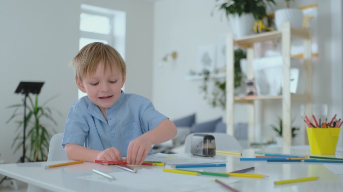 男孩坐在客厅的桌子上用铅笔在纸上画画