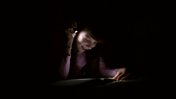 小女孩晚上在一间黑暗的房间里用手电筒看书