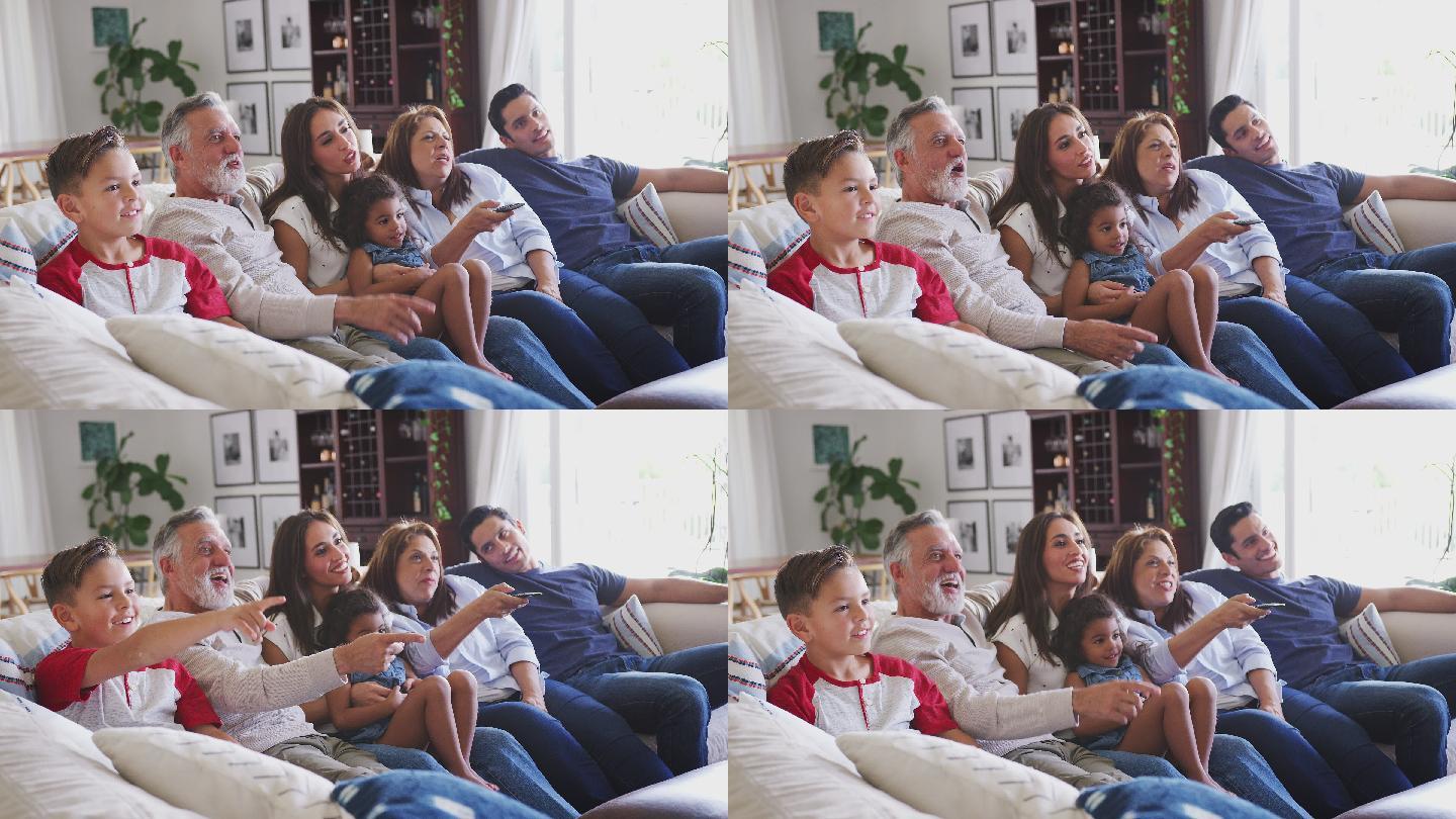 三代家庭坐在沙发上看电视，祖母用遥控器