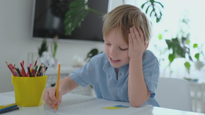 穿着蓝色t恤的男孩坐在厨房的桌子旁画东西