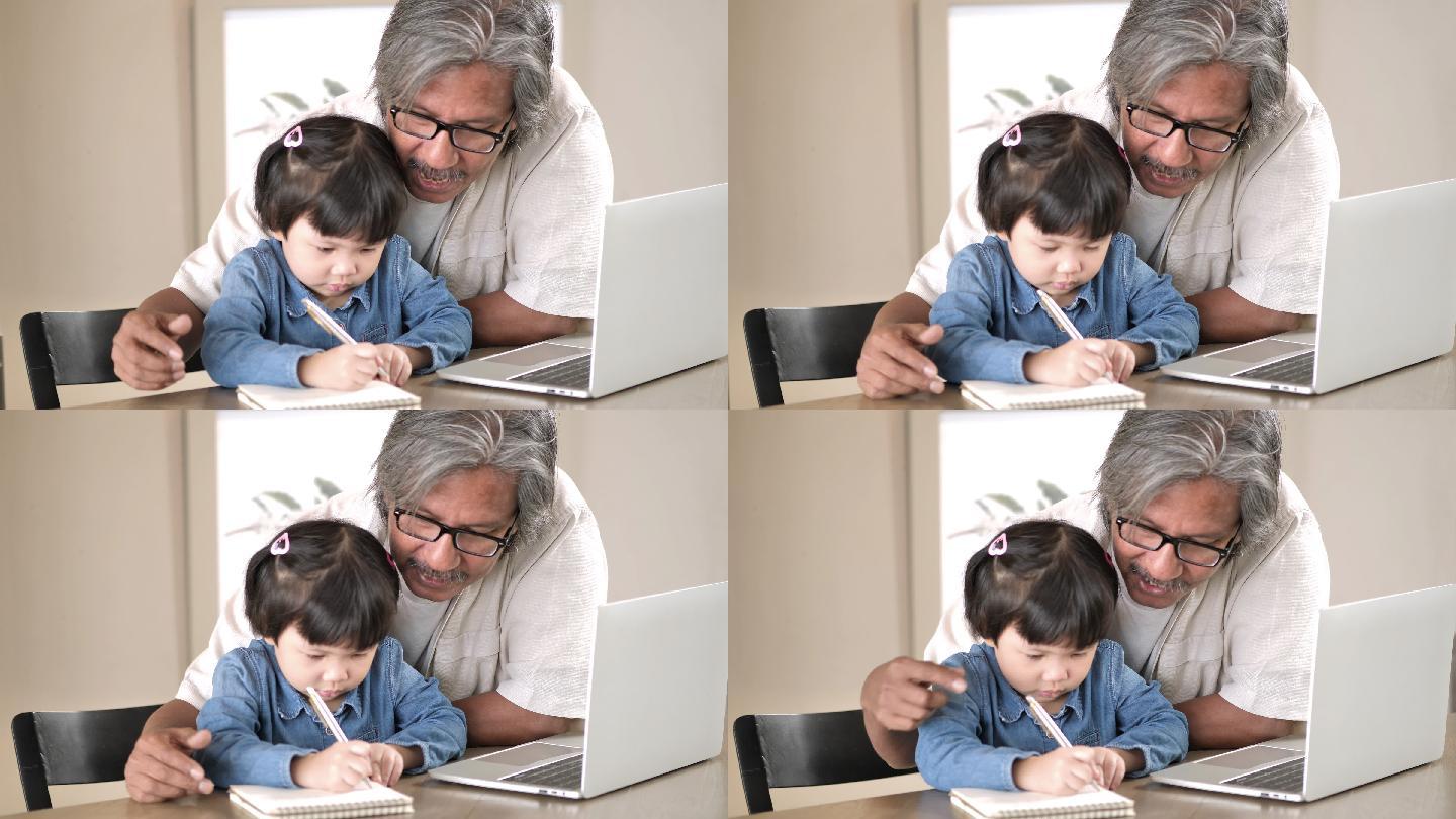 祖父和孙女在家里一起写字和使用笔记本电脑