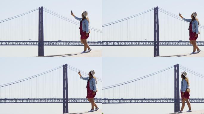 女孩戴着帽子在桥上用手机自拍