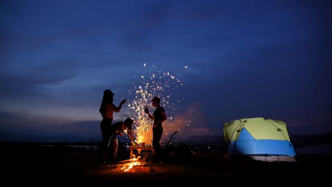 朋友在湖边一起在帐篷前篝火和玩烟花