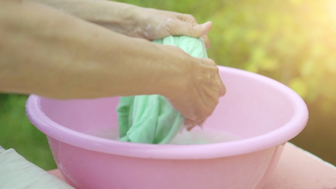 女人的手在一个粉红色的塑料碗里洗衣服