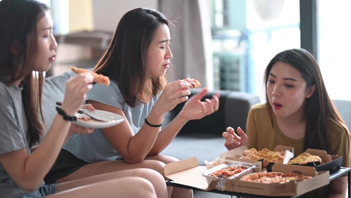 三位女性朋友在客厅吃披萨午餐