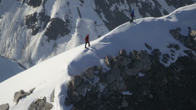 阳光下，两名登山者站在白雪覆盖的山上