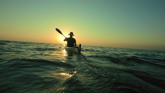 一个人戴着帽子在日落时皮划艇向地平线。