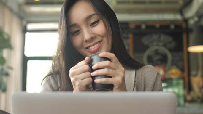 年轻女子看着笔记本显示器和咖啡杯