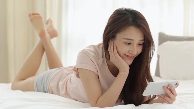 快乐的年轻女士在卧室玩手机