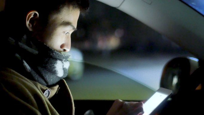 年轻的亚洲人在车里看手机