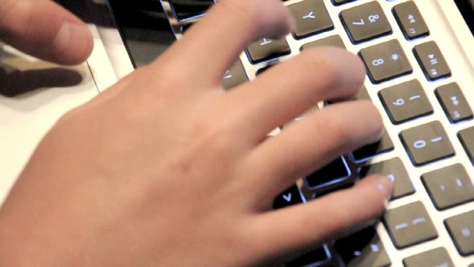 两只手在亮着的笔记本电脑键盘上打字。
