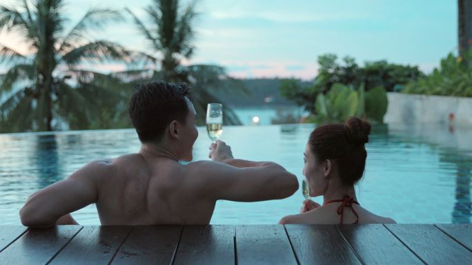 快乐的年轻情侣在泳池边喝香槟