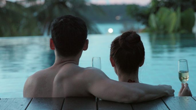 年轻情侣在泳池边喝香槟