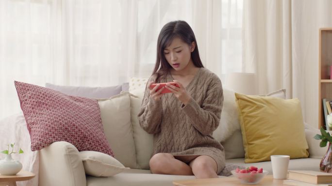 年轻女士在沙发上玩手机游戏