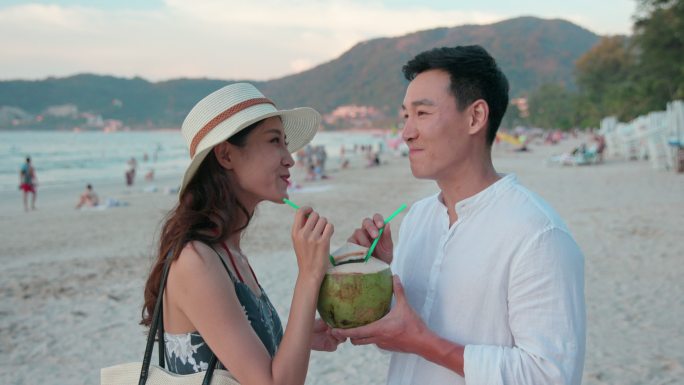 快乐的年轻情侣在沙滩喝椰汁