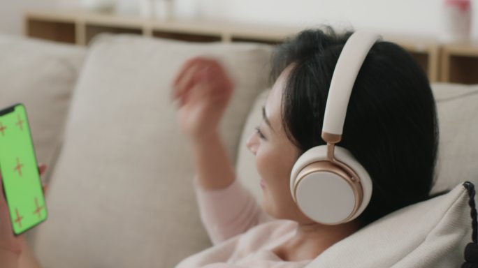 快乐年轻女士在家戴着耳机听音乐