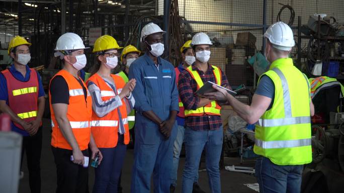 一群工厂工人戴着防护面罩在工业工厂开会