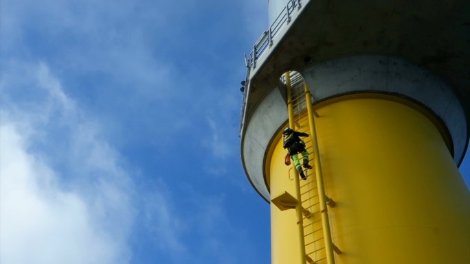 技术人员爬上最大风力涡轮机的梯子