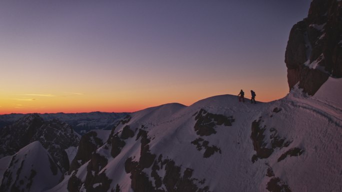 日出时，徒步旅行者在白雪覆盖的山脊上行走