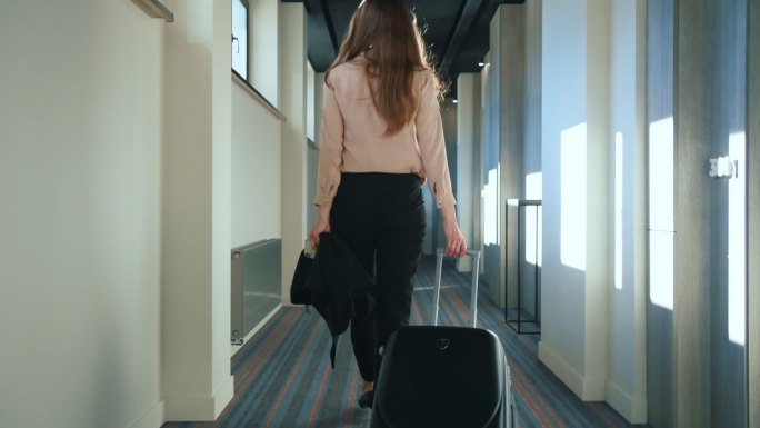 带着旅行箱在酒店走廊上行走的女人