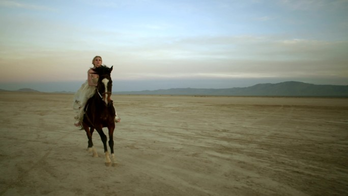 金发女郎骑着一匹马穿越沙漠