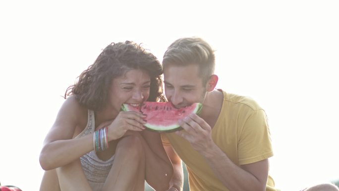 一对年轻夫妇在海滩上吃西瓜