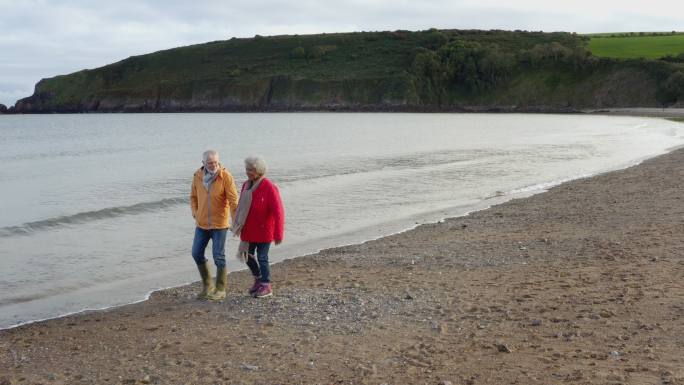 一对相爱的老年夫妇手牵着手沿着海岸线散步