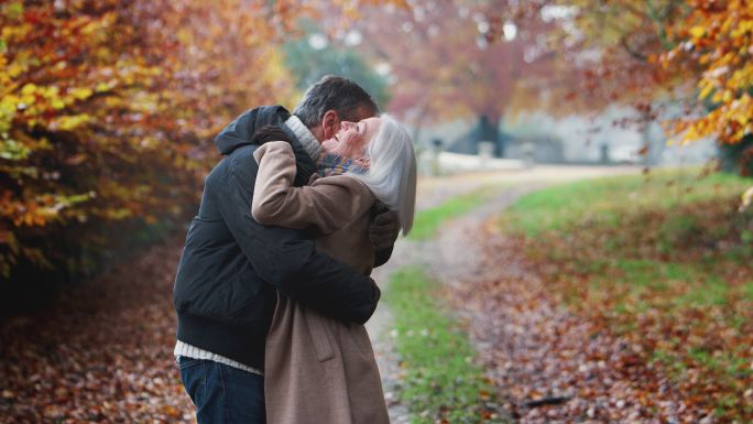 相爱的老年夫妇在秋天的乡间小路上拥抱