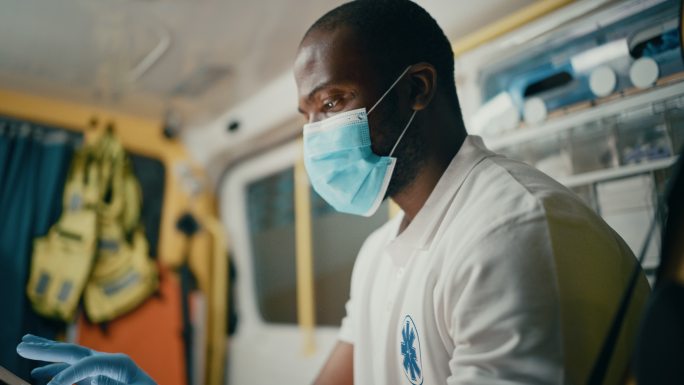 护理人员戴着口罩在救护车中使用平板电脑