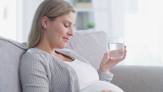 年轻孕妇在家里沙发上休息时喝水