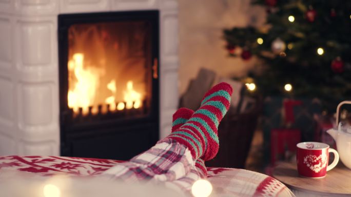 壁炉旁穿着舒适圣诞羊毛袜的女士脚，背景是装饰过的圣诞树和T恤杯