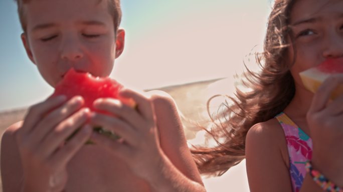快乐的男孩和女孩在海滩上吃西瓜