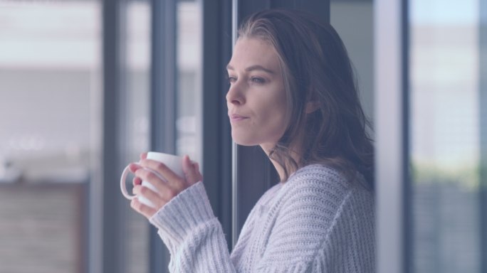 一个年轻女子站在家里的阳台上喝着一杯咖啡