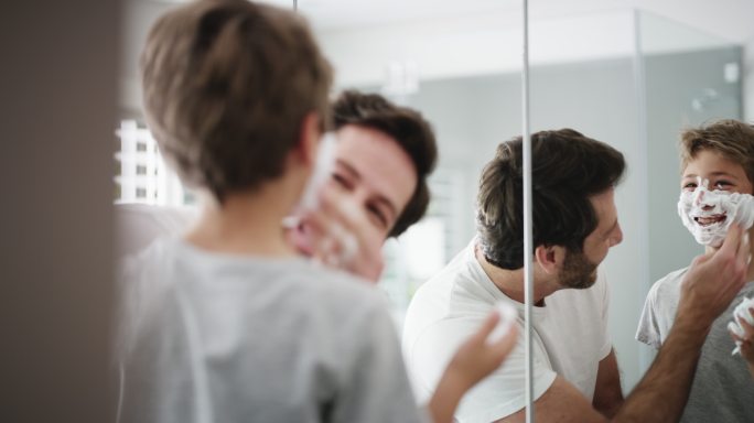 一位父亲在浴室里给儿子脸上抹剃须膏