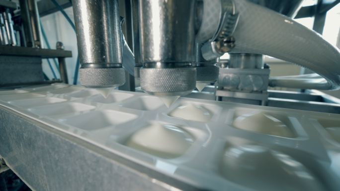 工厂机器用白色酸奶填充容器。
