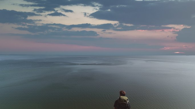 背着包的男人站在海景背景的山崖上