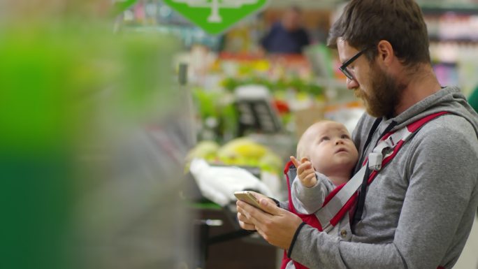 一名男子带着孩子在超市使用智能手机