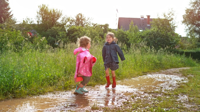 两个小女孩穿着雨靴在泥泞的水坑里跳