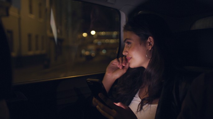 女子夜间在城市的一辆汽车上使用智能手机
