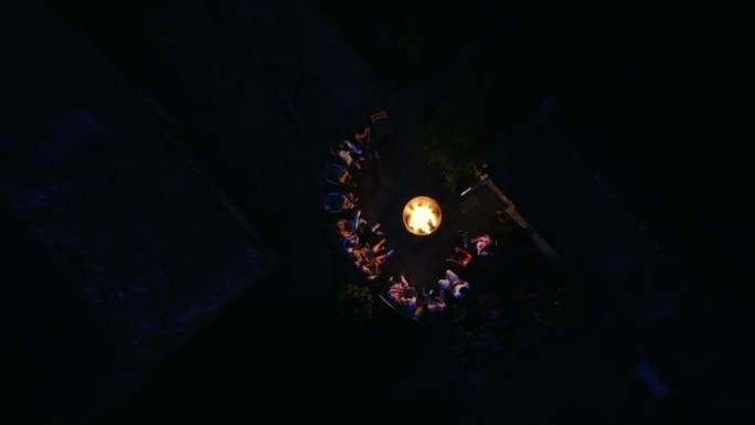 一群朋友围坐在火堆旁，鸟瞰全景。