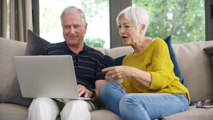 一对老年夫妇在家沙发上使用笔记本电脑