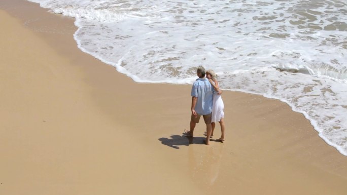 老年夫妇一起走在沙滩上，高角度观看