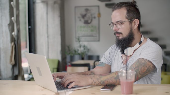 一个留胡子的男人坐在咖啡馆里用他的电脑。