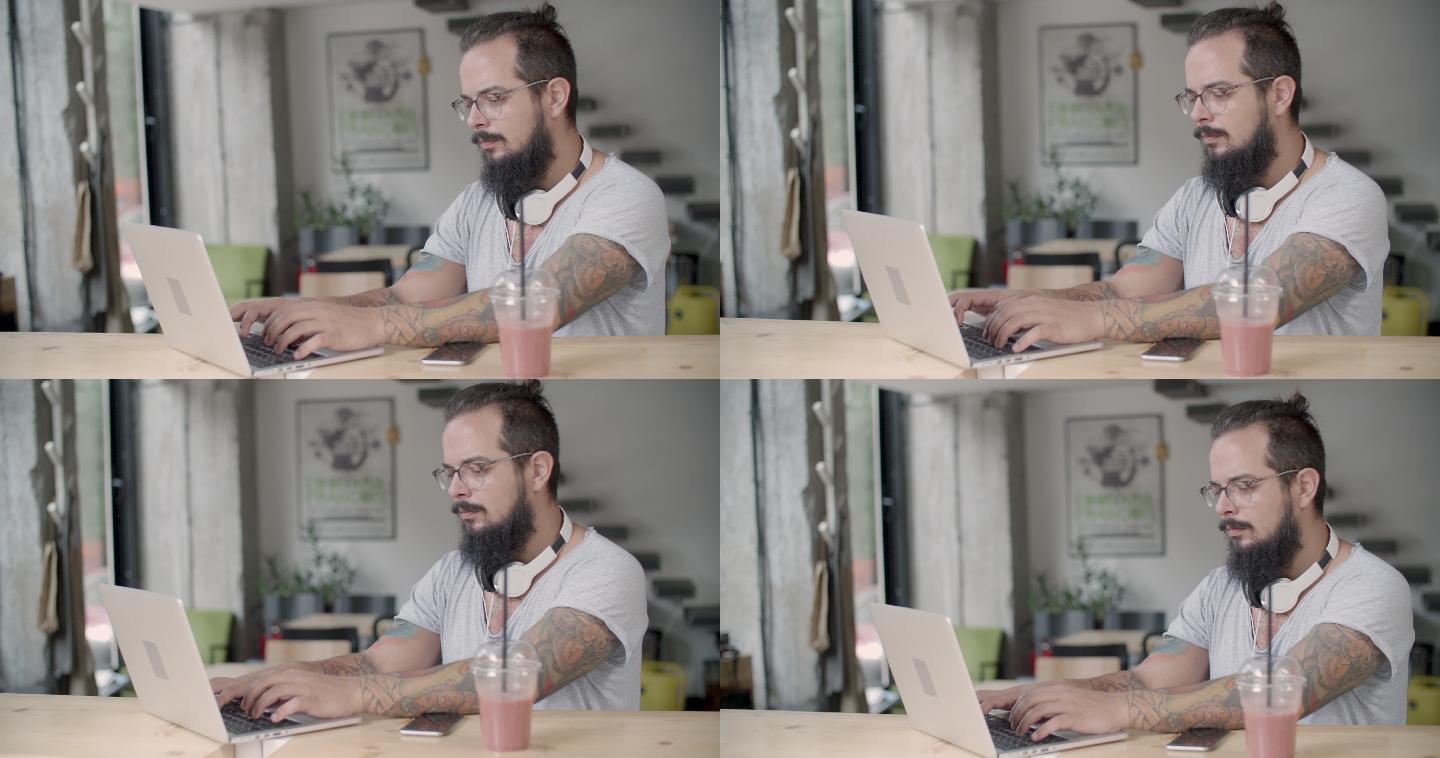 一个留胡子的男人坐在咖啡馆里用他的电脑。