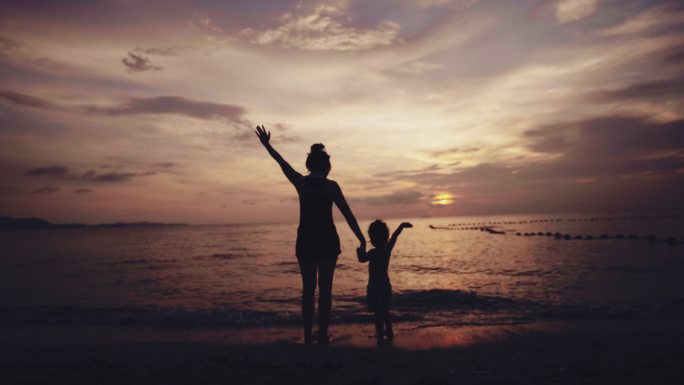 海滩上的幸福家庭母女站在海边挥手告别夕阳