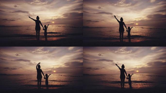 海滩上的幸福家庭母女站在海边挥手告别夕阳