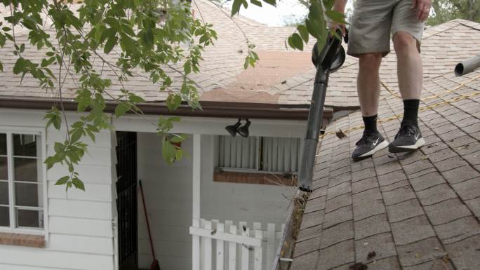 使用电动吹叶机清除家中铝制屋顶排水沟