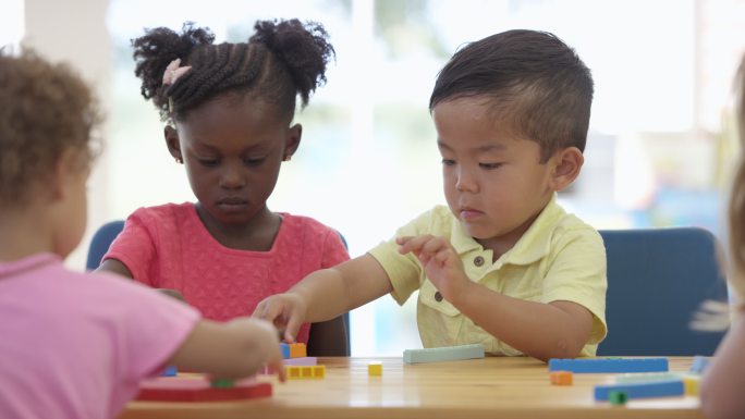 三个儿童在一张桌子旁一起搭建玩具积木。